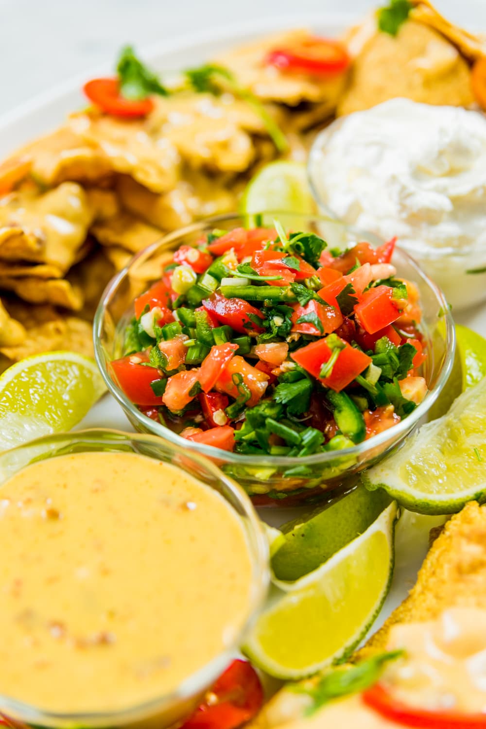 Glass container filled with homemade pico de gallo sitting on platter surrounded my stadium nachos