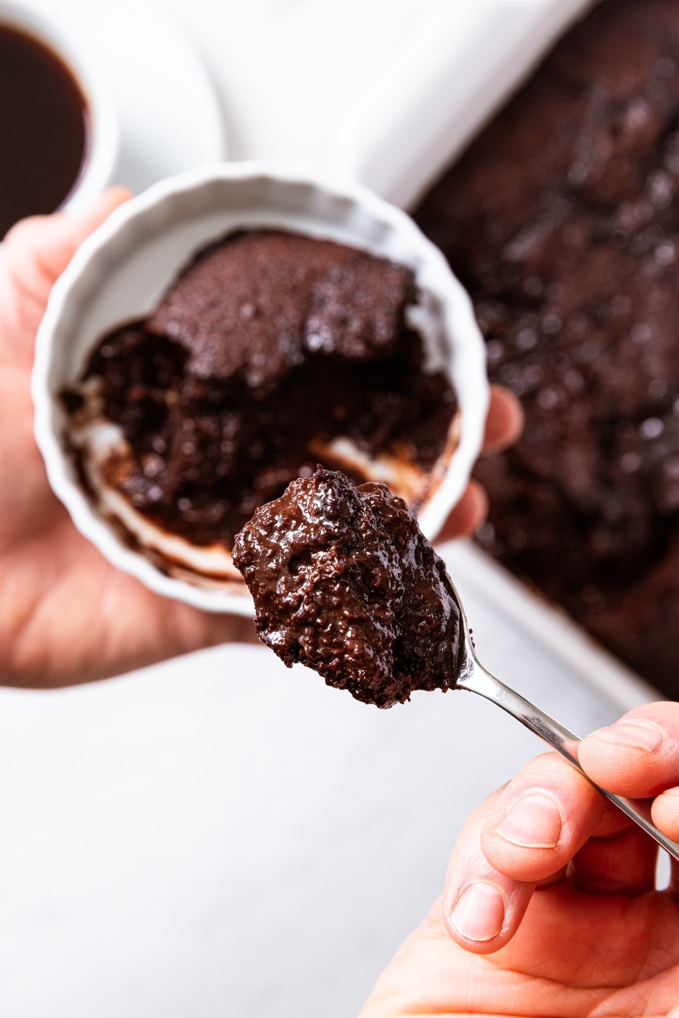 Hand holding spoon scooping chocolate pudding cake out of round bowl filled with a serving of chocolate cake.