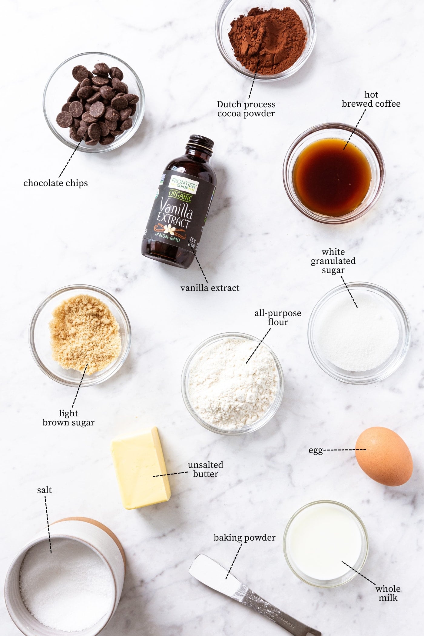White marble surface filled with all ingredients needed to make chocolate fudge cake with brown sugar, white sugar, butter, sugar, milk, chocolate, and more.
