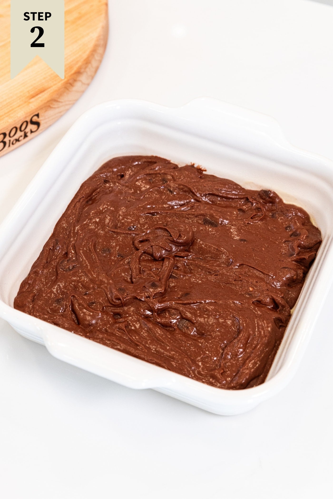 White square baking dish filled with chocolate batter needed to make chocolate fudge pudding cake sitting on white countertop.
