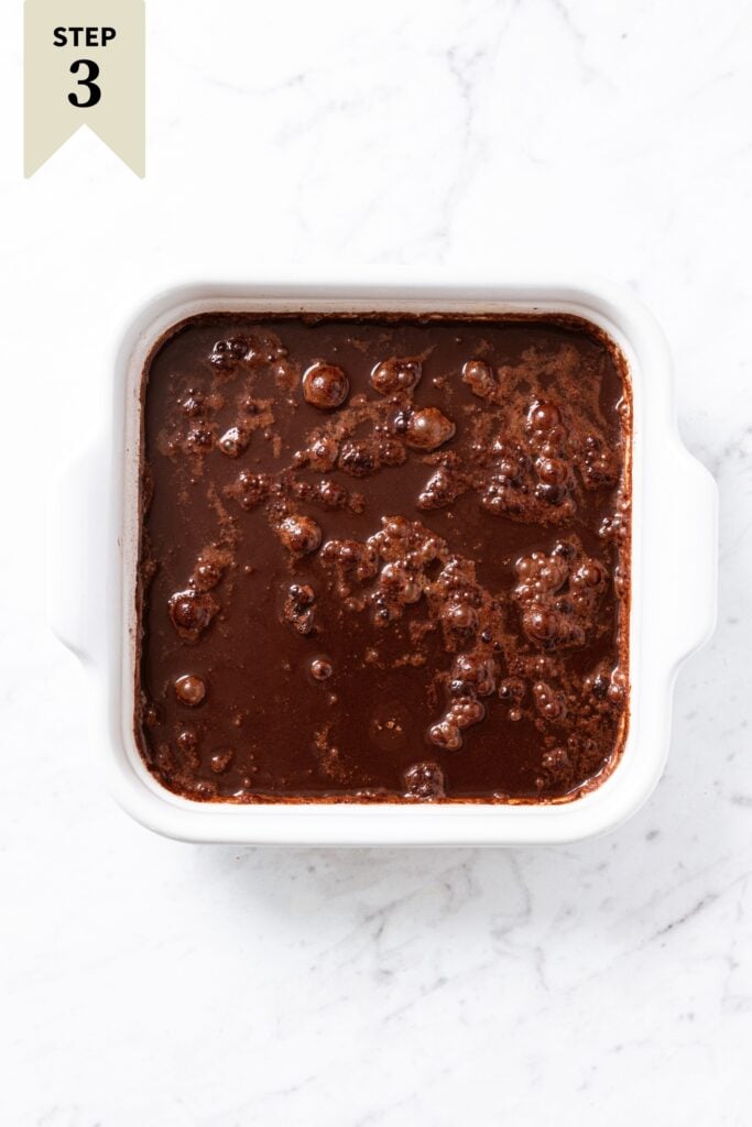 Unbaked chocolate fudge pudding cake with liquid all over the top sitting on white marble surface right before being baked.