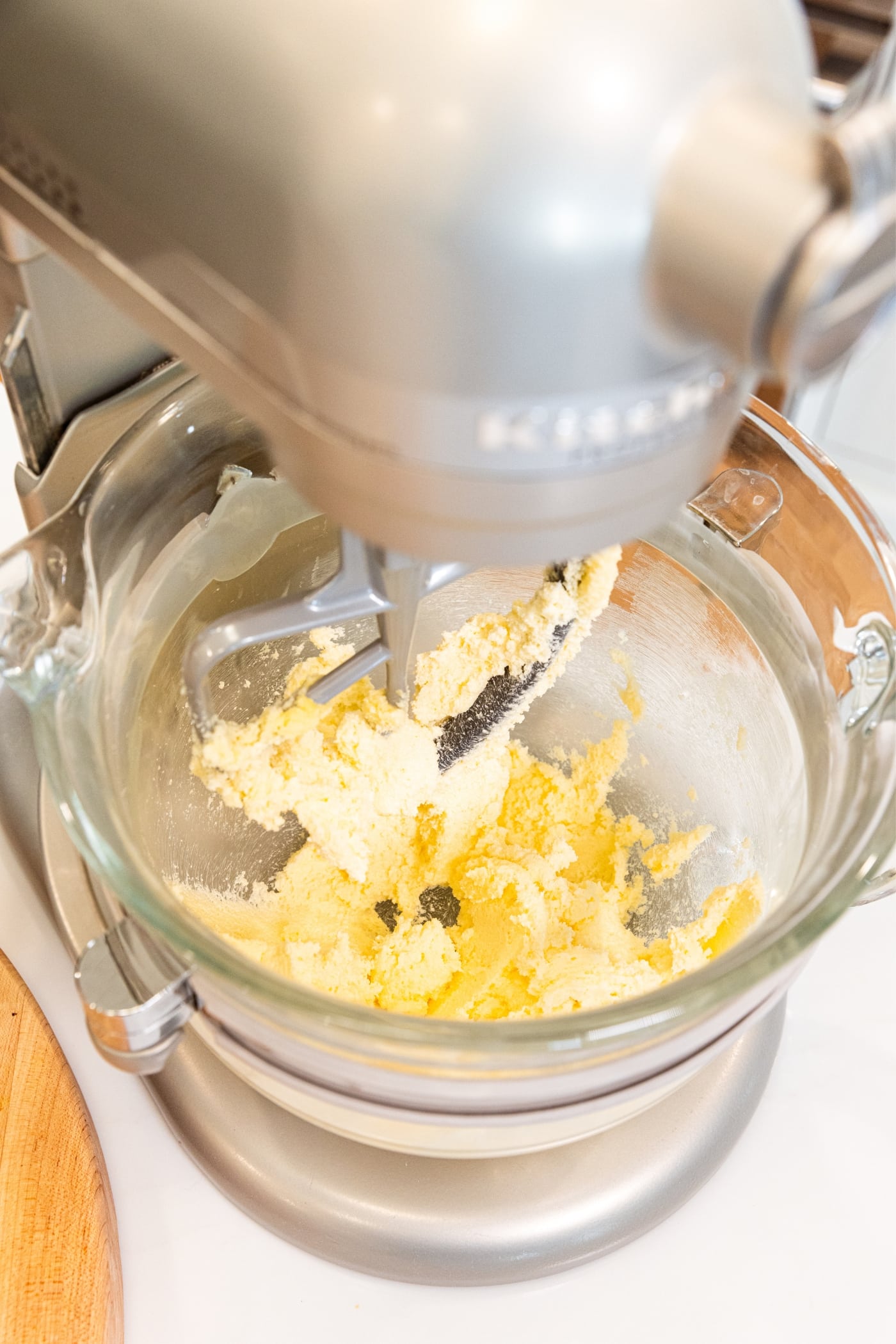 Glass bowl on stand mixer mixing together butter and granulated sugar sitting on white countertop.
