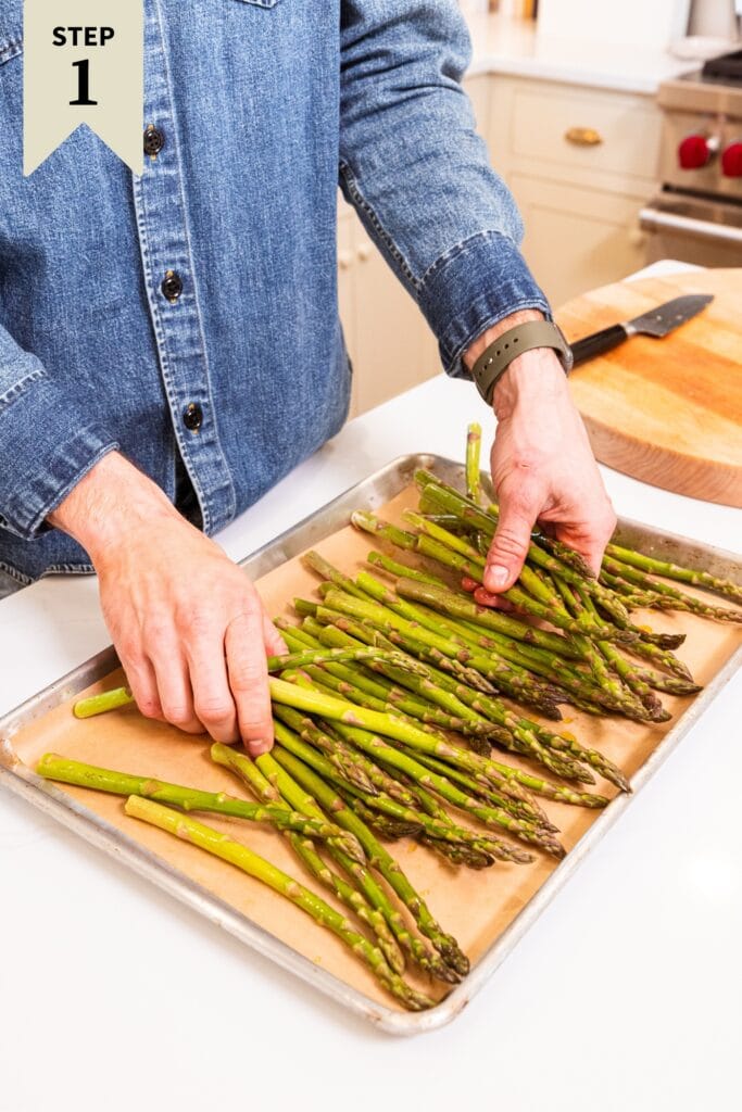 Two hands tossing pieces of asparagus with olive oil and salt and black pepper before roasting.