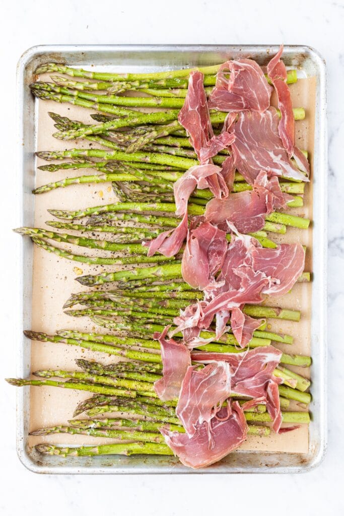 Pieces of asparagus on a parchment-lined baking sheet before going into the oven to roast.
