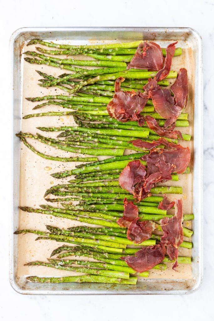 Pieces of roasted asparagus topped with prosciutto right after coming out of the oven.