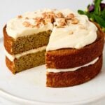 White cake plate with banana cake on top with mascarpone frosting and crushed banana chips.