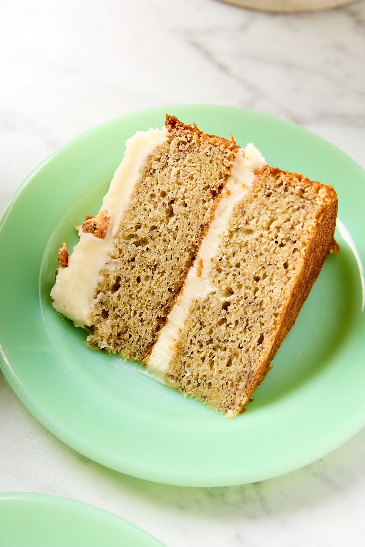 Green plate with slice of brown butter banana cake with frosting.