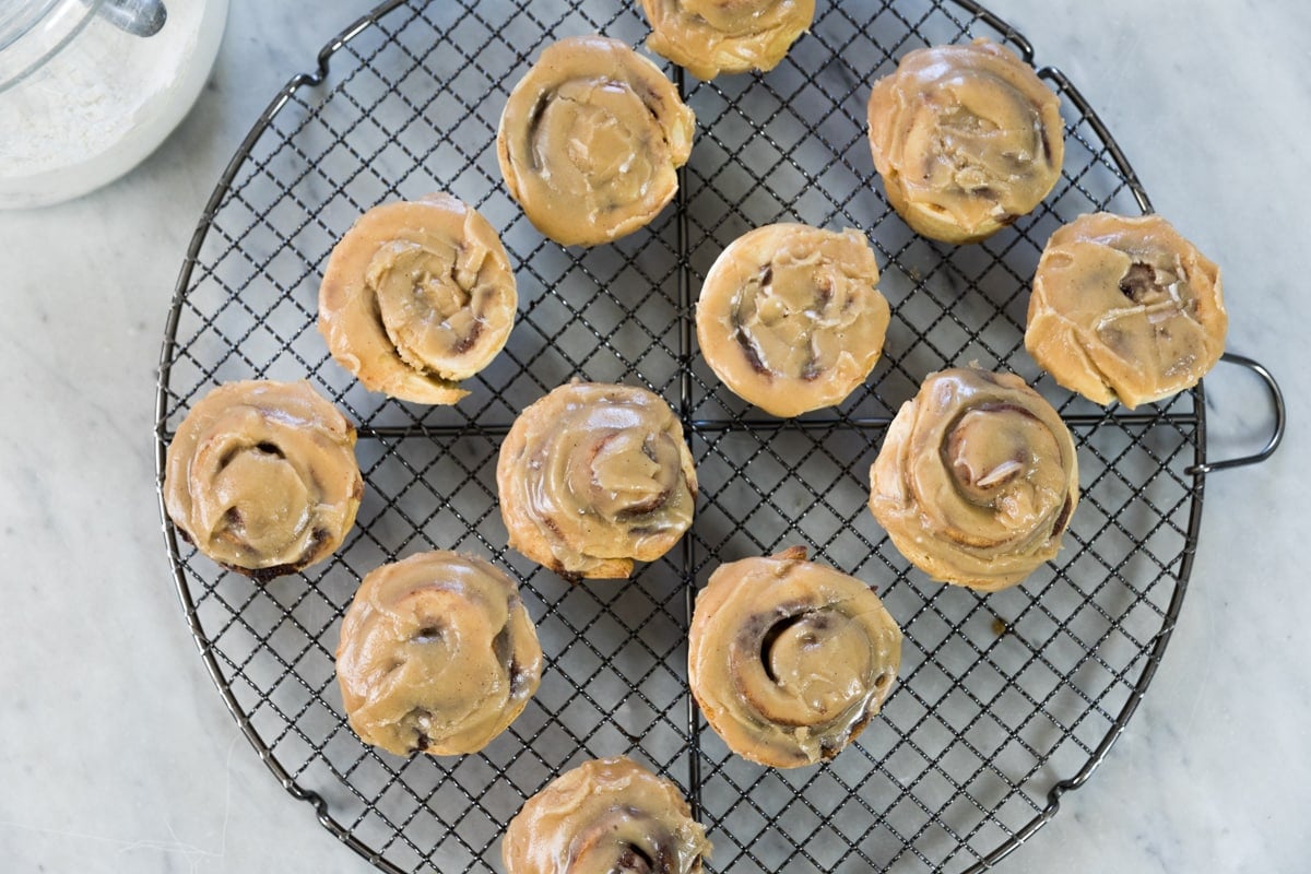 Top down view of circular cooling rack holding cooling cinnamon roll muffins topped with brown sugar glaze