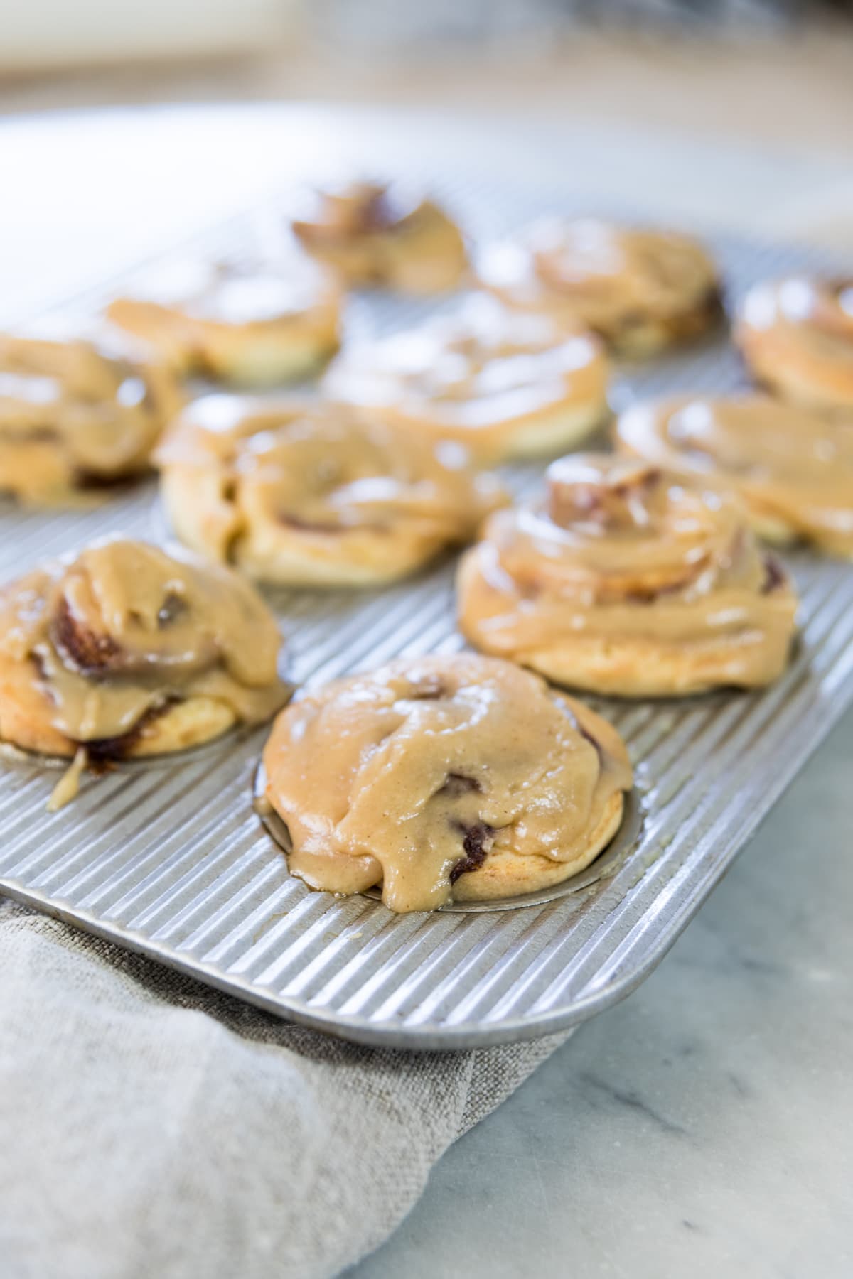 Silver muffin tin filled with cinnamon roll muffins swirled with cinnamon and glazed with a brown sugar icing
