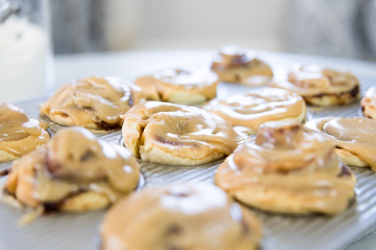 Silver muffin tin filled with cinnamon roll muffins filled with cinnamon filling and topped with brown sugar glaze