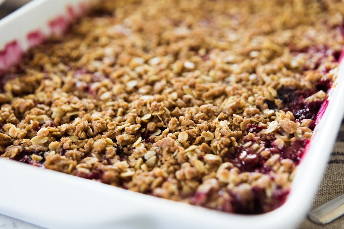 White baking dish sitting on countertop showing oat crumble topping on top of berry crisp