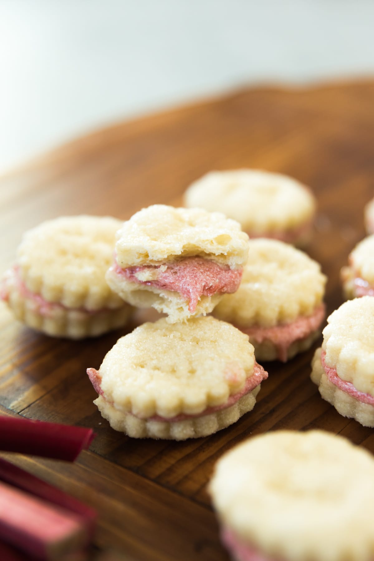 Light brown rhubarb wafer cookie broken in half with light pink frosting spilling out with extra rhubarb stalk on top of wood bread board