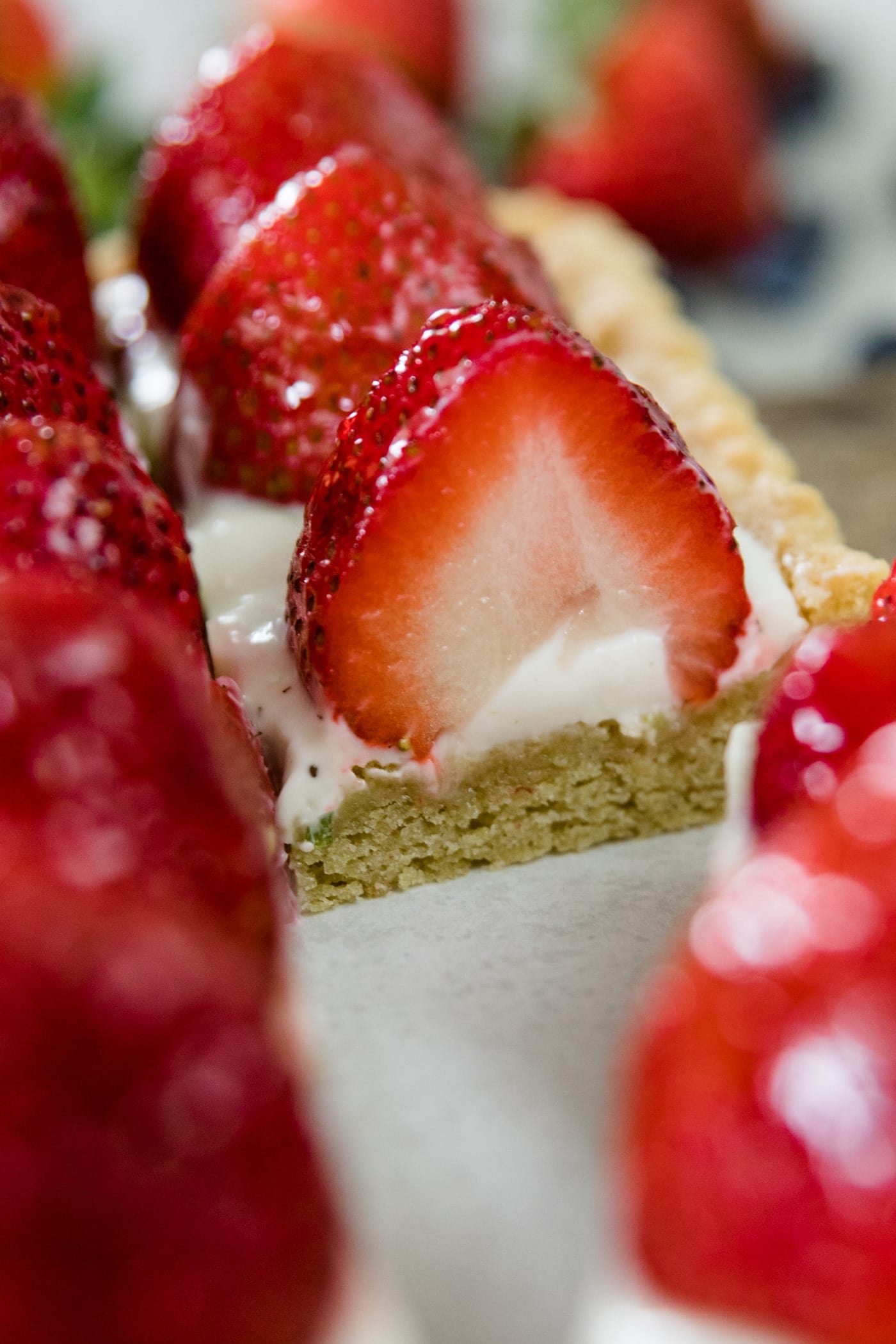 Cut piece of strawberry and blueberry cookie tart with half strawberry showing on top of a yogurt filling on a wood cutting board lined with parchment paper on a marble surface