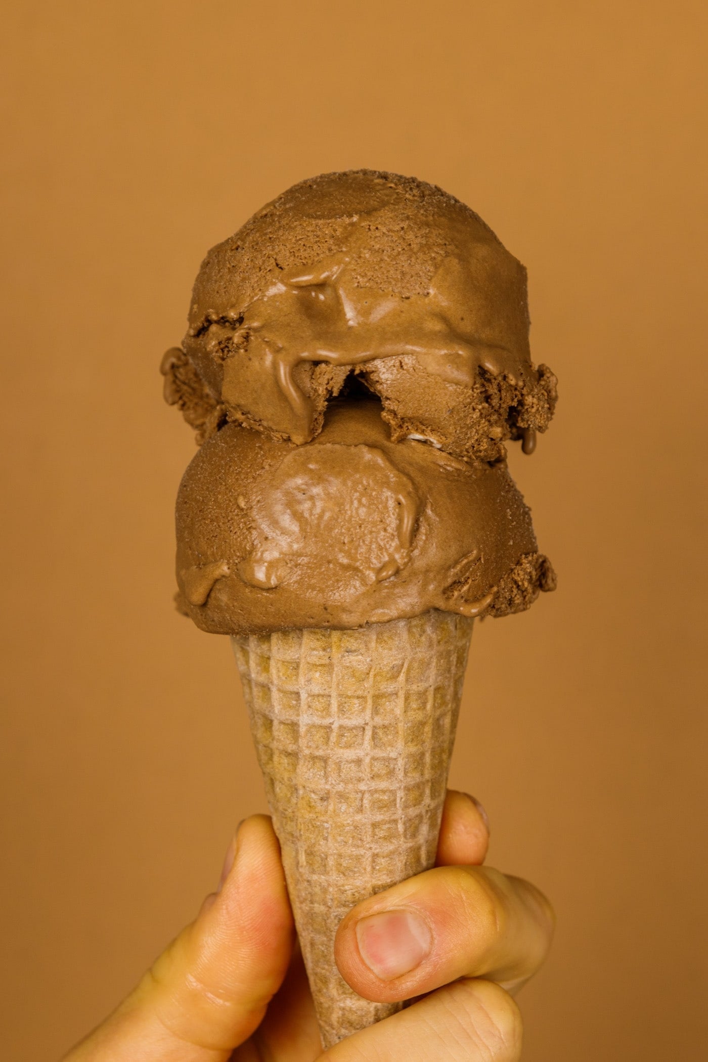 Two scoops of French silk pie ice cream on an ice cream cone held by a hand with a brown background