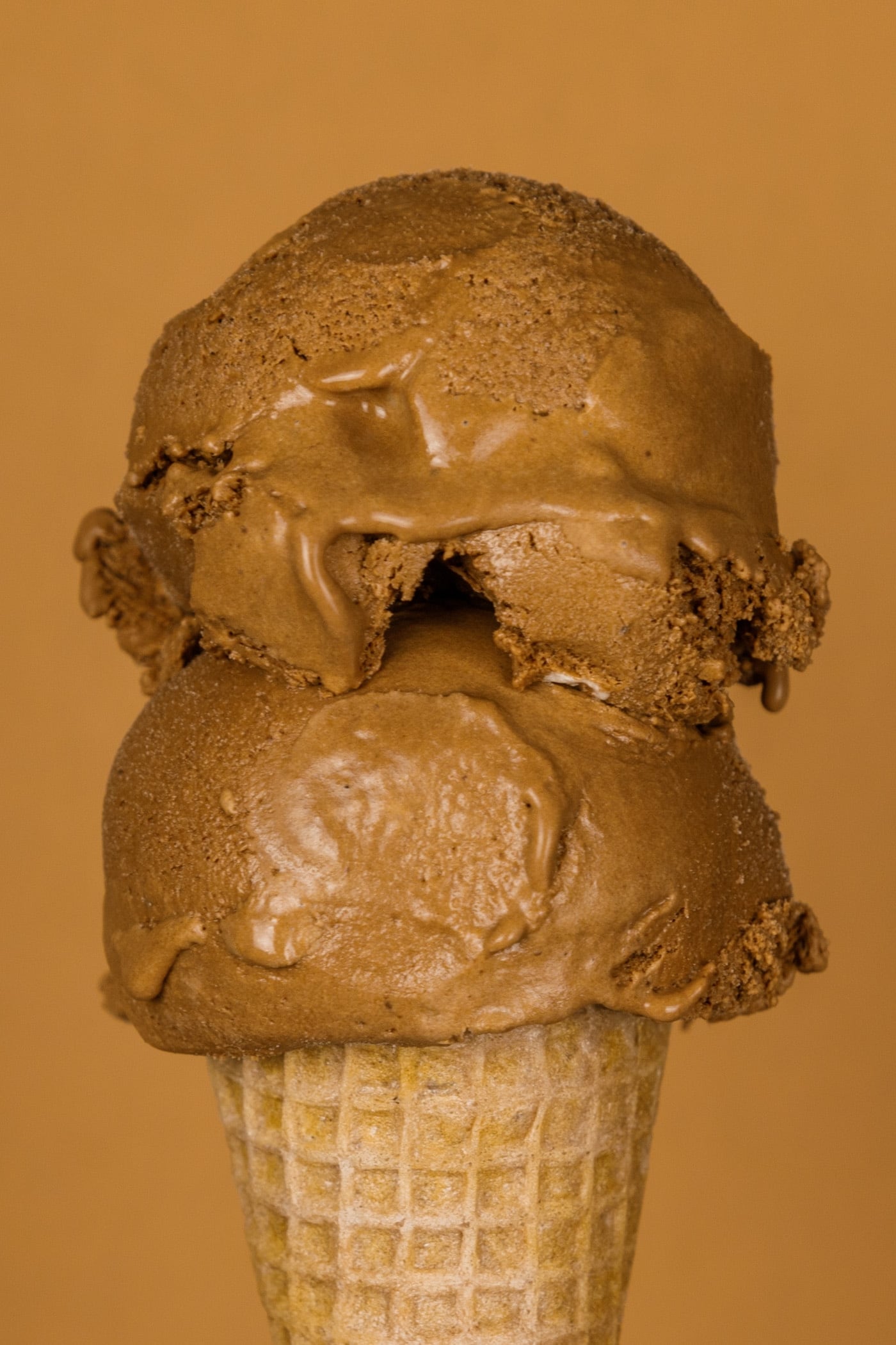 Two scoops of French silk pie ice cream on an ice cream cone with a brown background