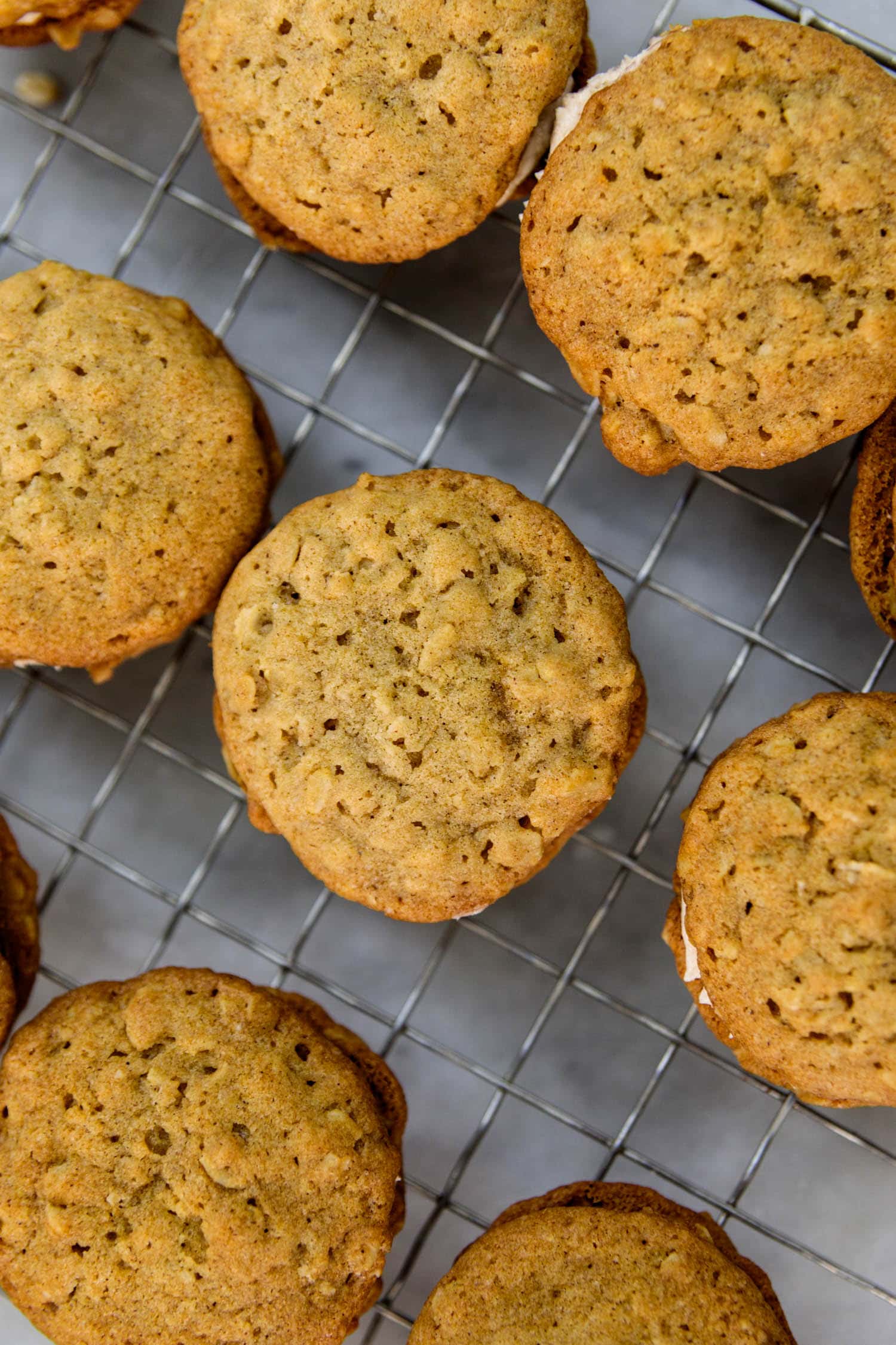 Top down view of oatmeal spice creme-filled cookies all on a wire cooling rack on a marble surface