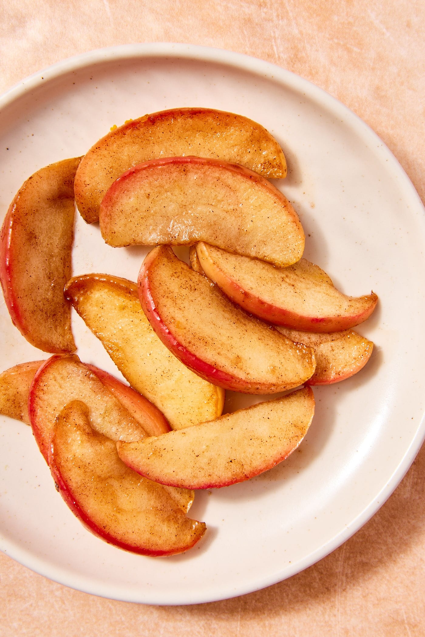 White plate filled with cinnamon covered cooked apples sliced into wedges.