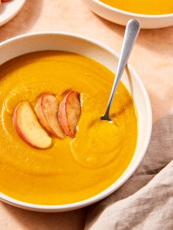 White bowl filled with orange colored slow cooker squash soup with slices of cooked apple on top.