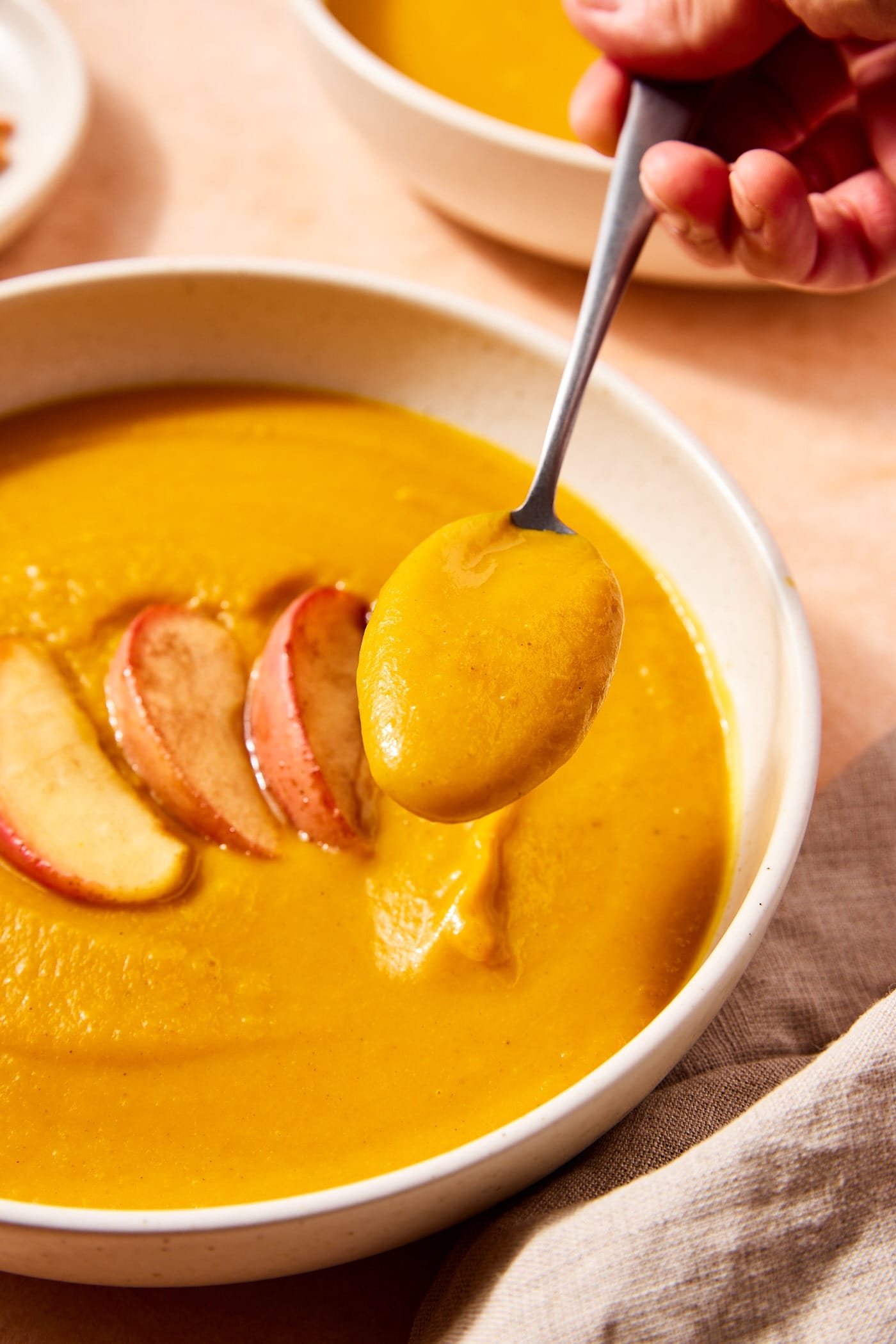 Spoon holding serving of slow cooker squash soup with rest of soup in bowl below.