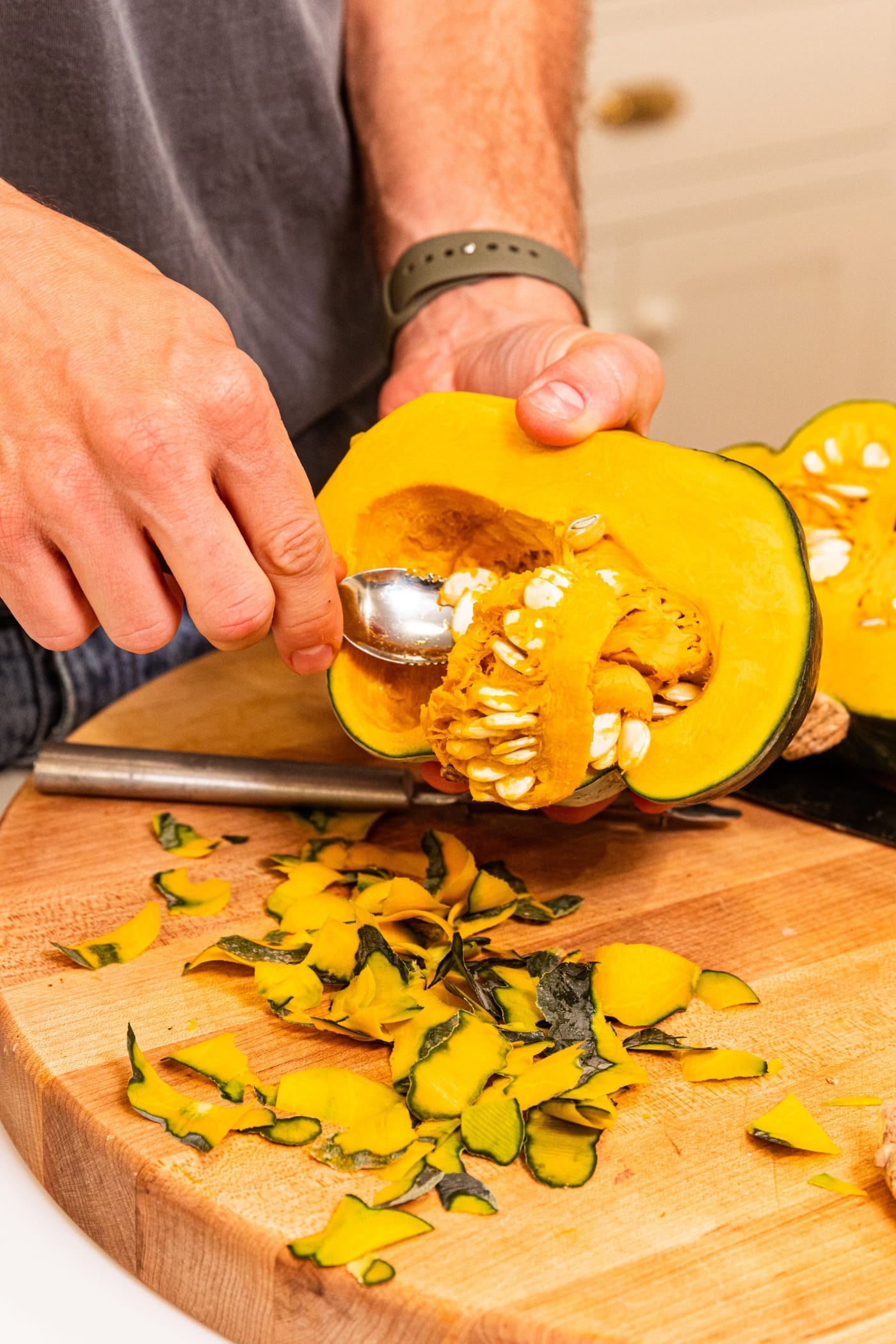 Hand holding onto sliced squash scooping out the interior texture with a grapefruit spoon.