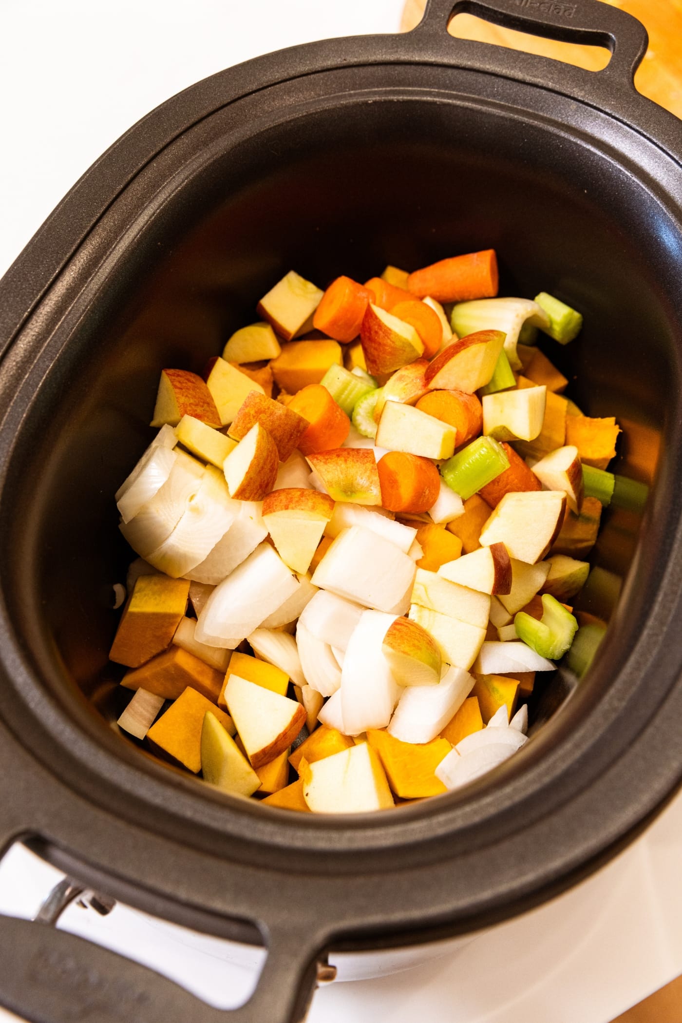 Slow cooker filled with sliced squash, apples, onion, celery, and more.