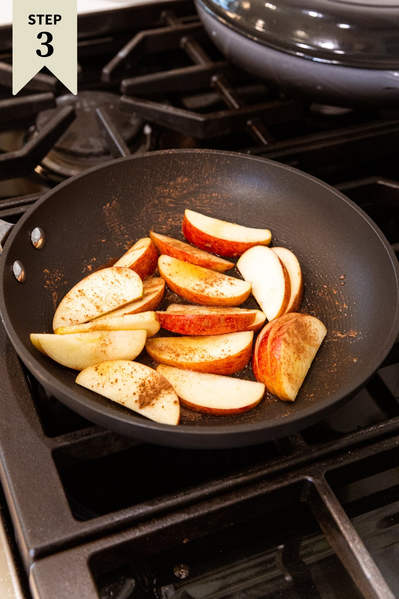 Skillet sitting on stovetop with sliced apples sprinkled with cinnamon and maple syrup.