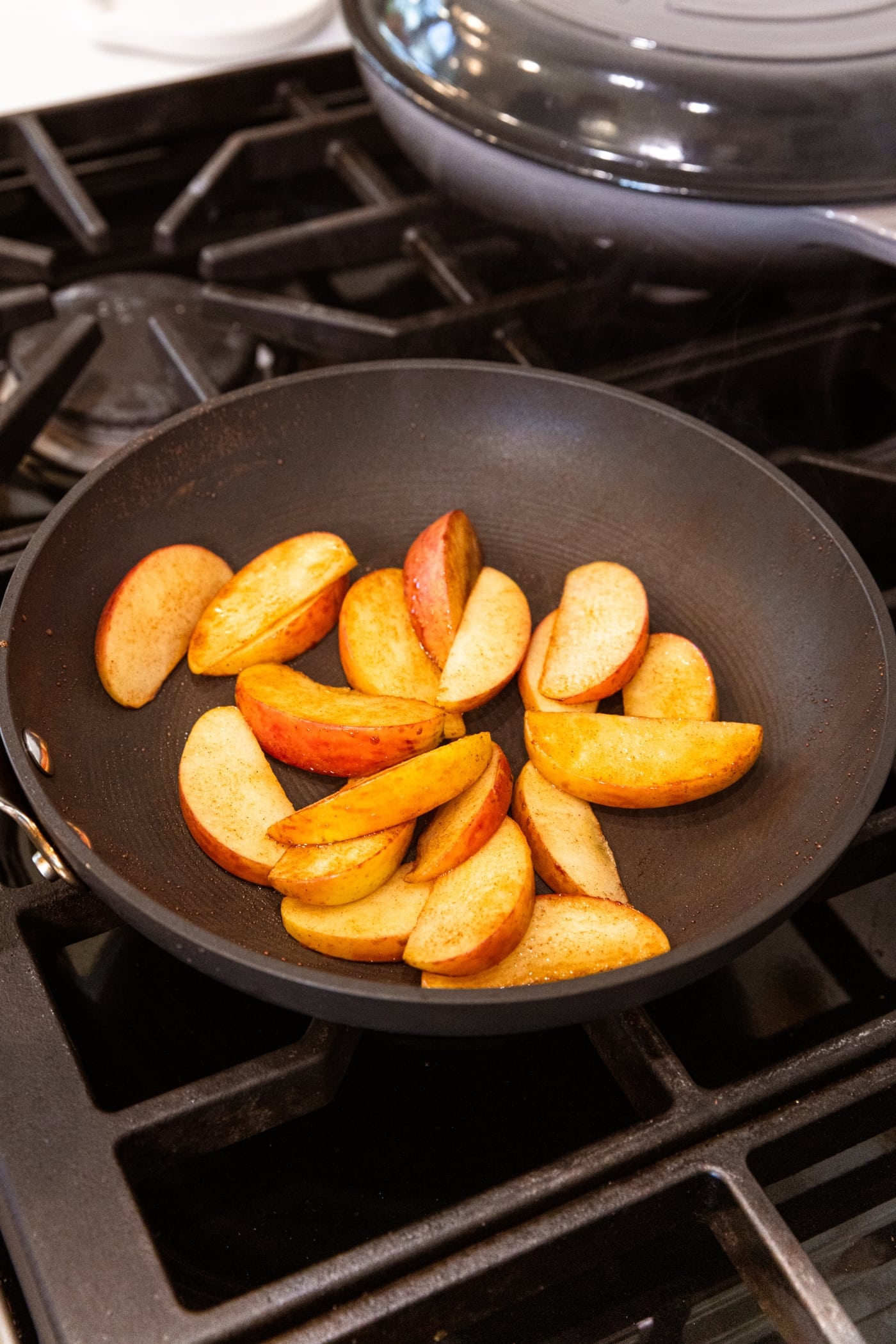 Skillet on stovetop with cooked apples with maple syrup and cinnamon on top.