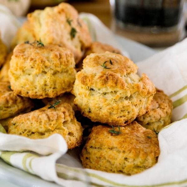 Herb cheese biscuits sitting on white and green towel in bowl with dishware surrounding all on white surface
