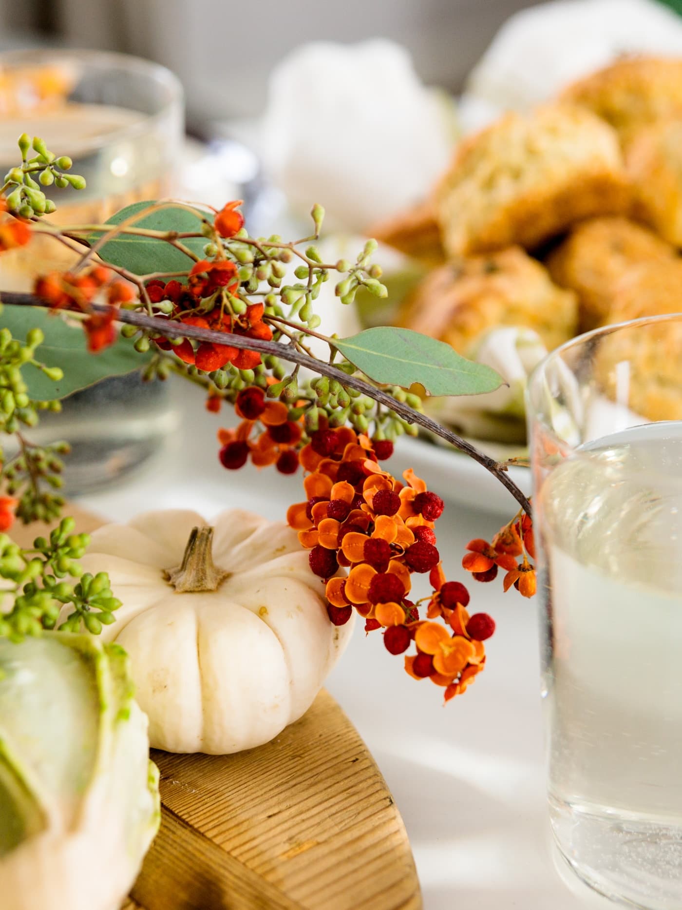 Herb cheese biscuits in background with bittersweet arrangement and white pumpkins in foreground all on white surface