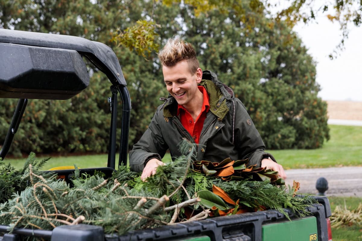 Kaleb Wyse wearing coat outdoors getting greens for outdoor Christmas decor from the back of a work vehicle.