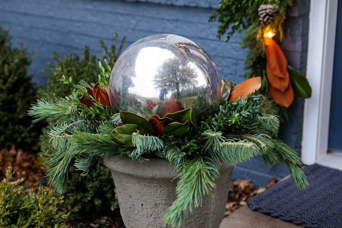 Silver gazing ball perched on top of greens and magnolia leaves in an urn for Christmas holiday decor.