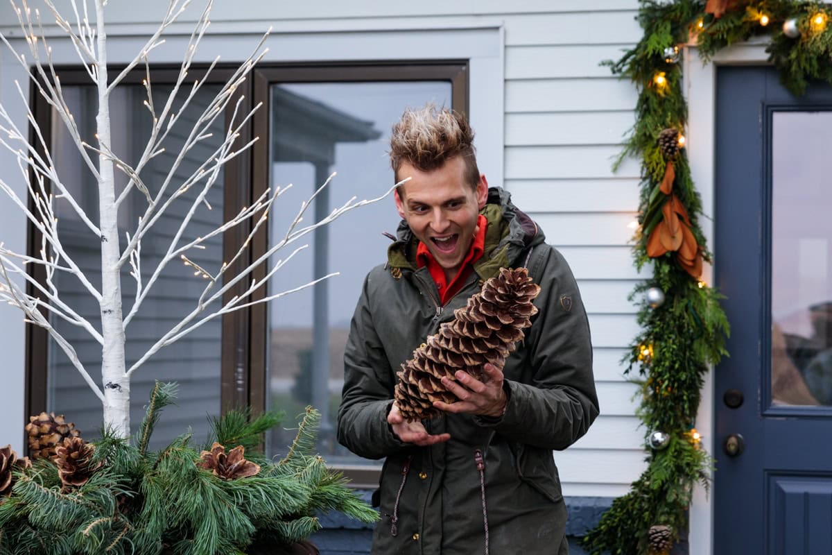 Kaleb Wyse holding a huge pinecone about to place it outside for some outdoor Christmas decor with a shocked look on his face.