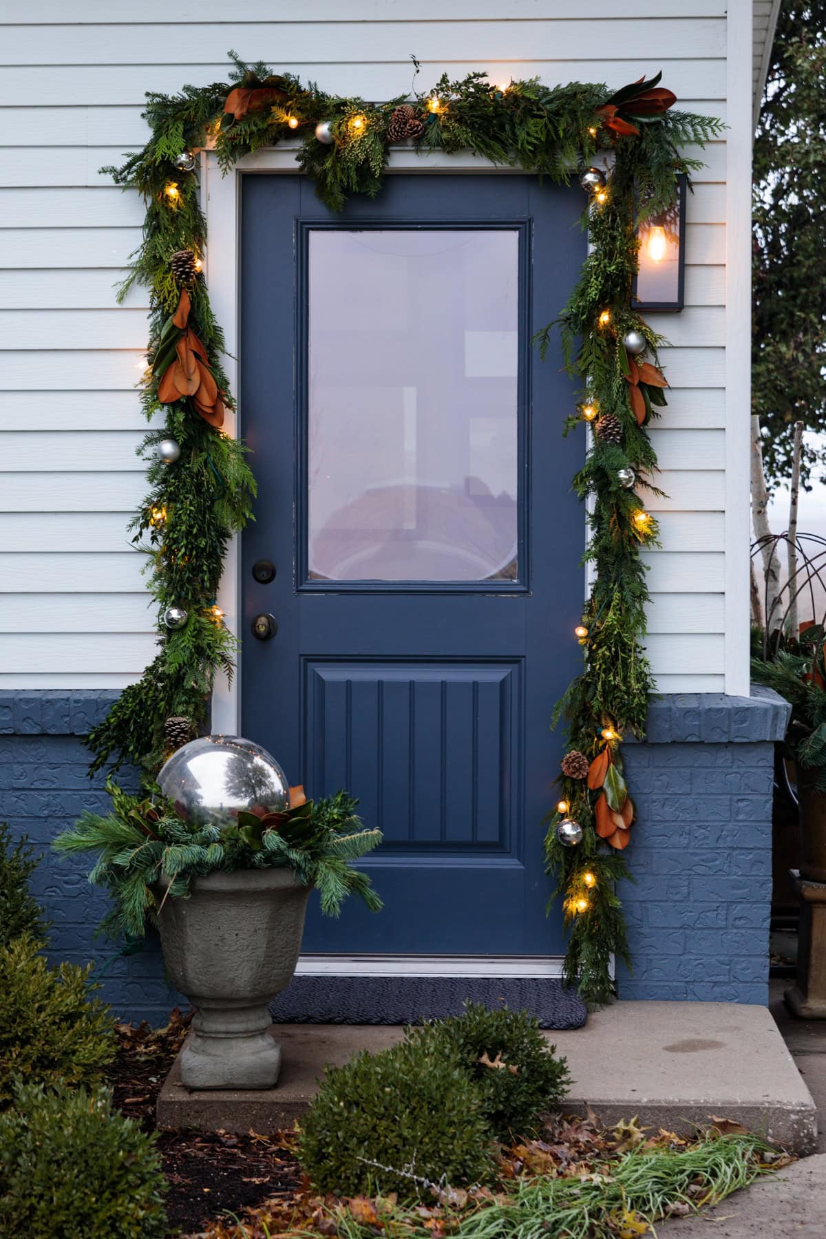 A blue front door adorned with garland all around with magnolia leaves and lights worked in as well.