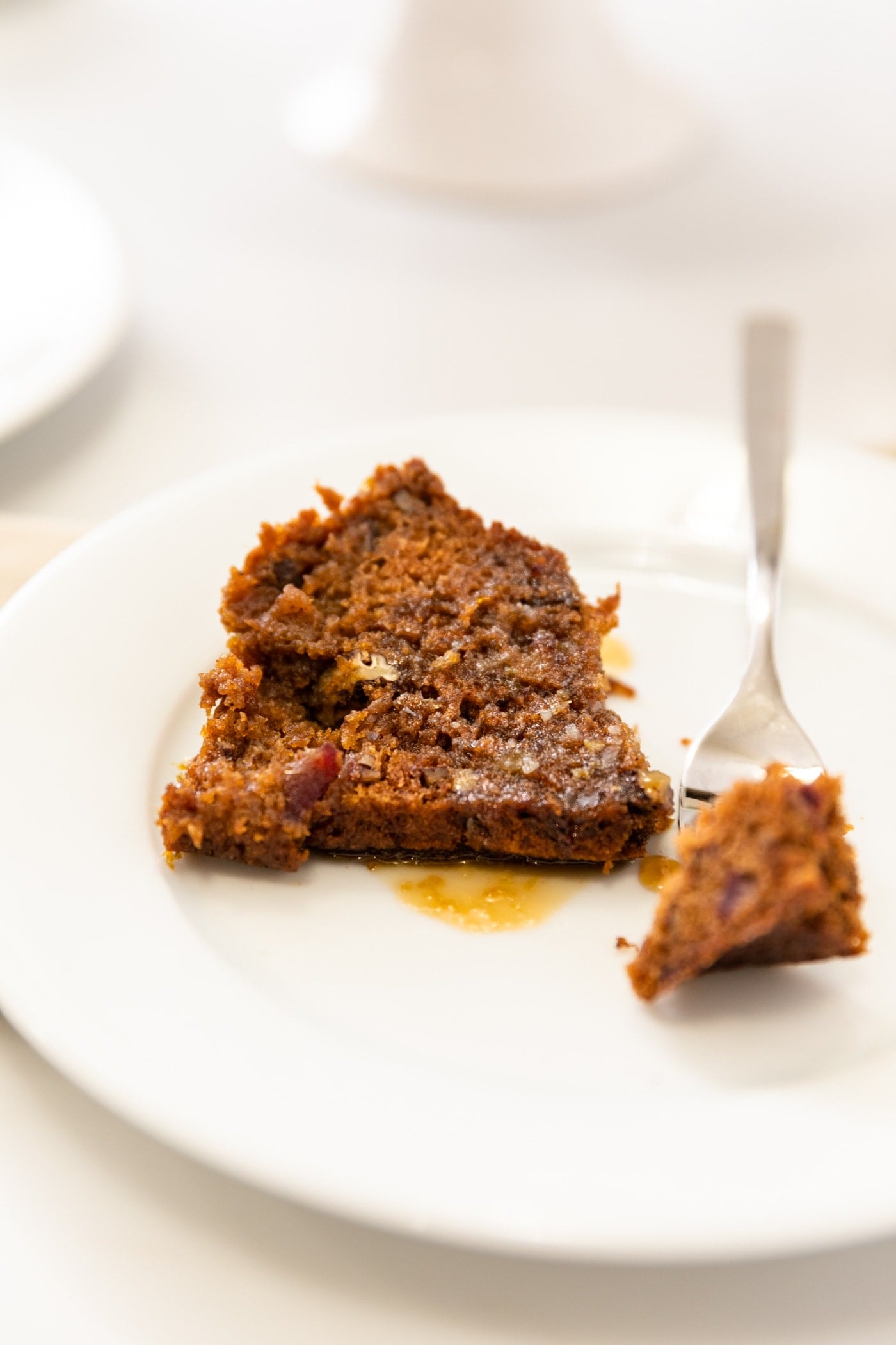 Piece of date pecan cake sitting on white plate with fork holding piece all on white surface