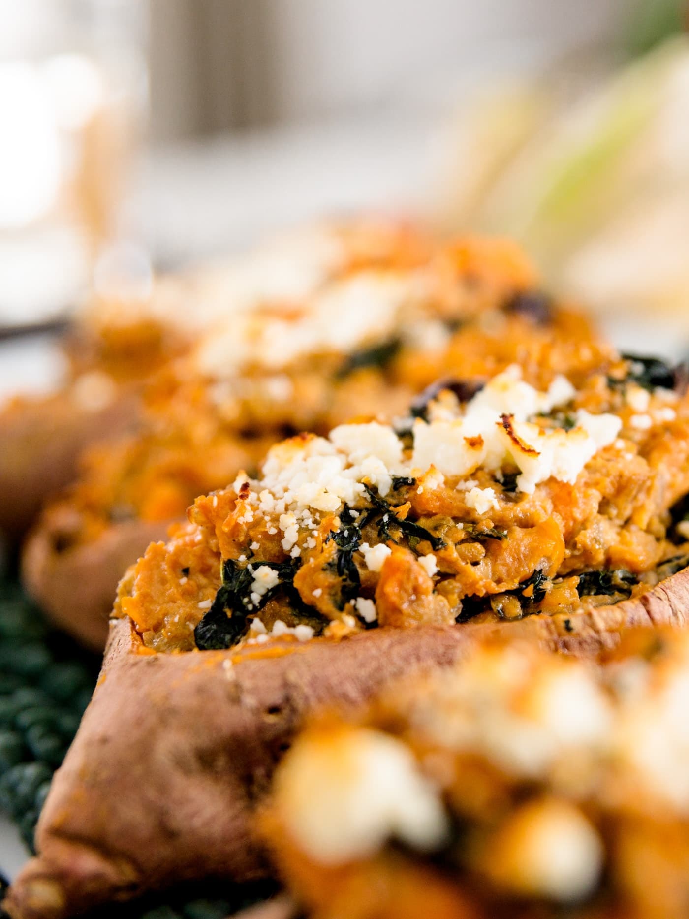 Twice baked sweet potatoes sprinkled with cheese and dotted with kale sitting on bed of kale with pumpkin in background on white surface