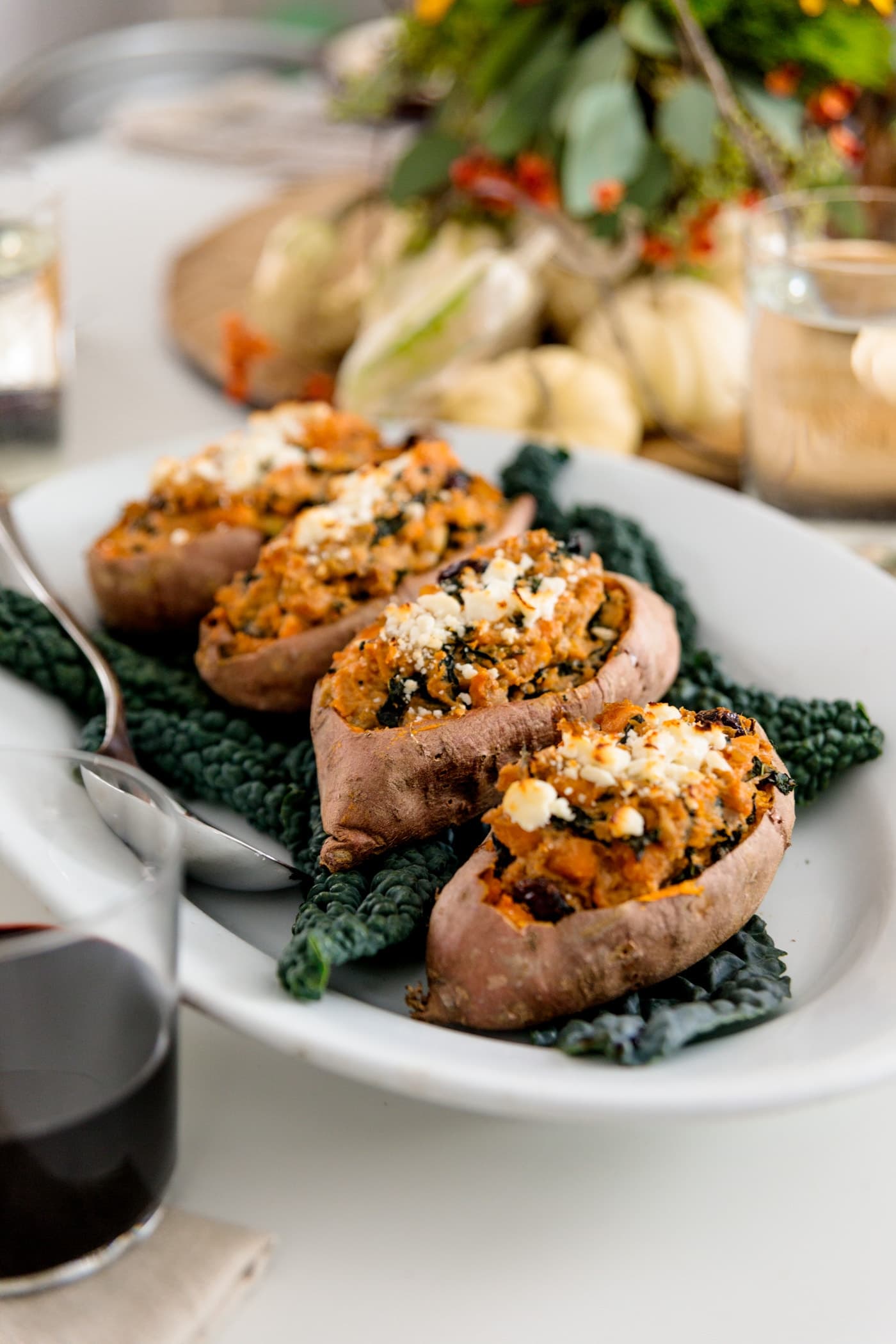 Twice baked sweet potatoes on bed of kale sitting on white plate with white pumpkins in background on white surface