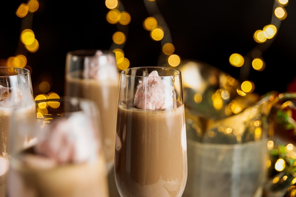 Yellow twinkling lights against black background with champagne flute filled with pink ice cream and chocolate coffee cooler in foreground