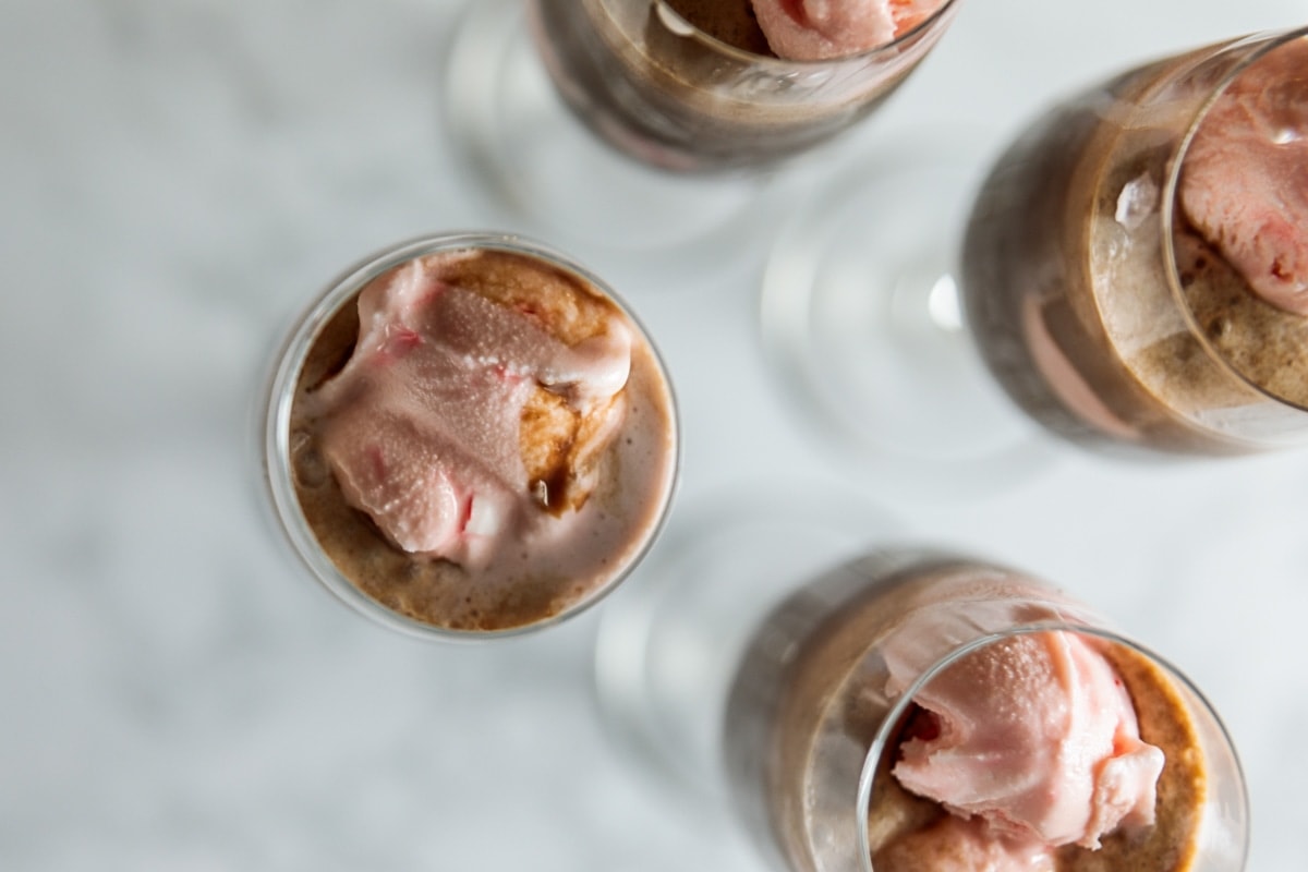 Top down view of champagne flutes filled with brown chocolate liquid with pink ice cream floating all on marble surface
