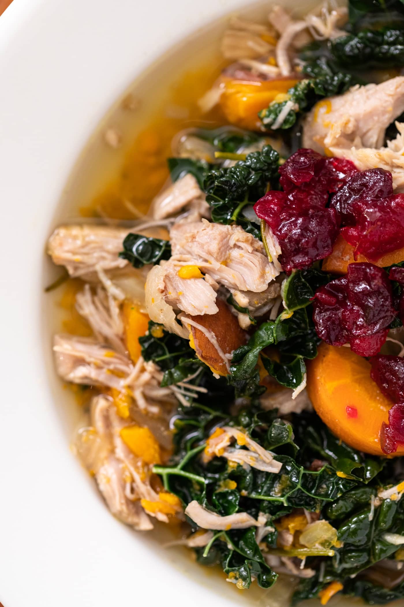 Close up top down view of turkey soup with kale and sweet potatoes and topped with a red cranberry sauce all in white bowl