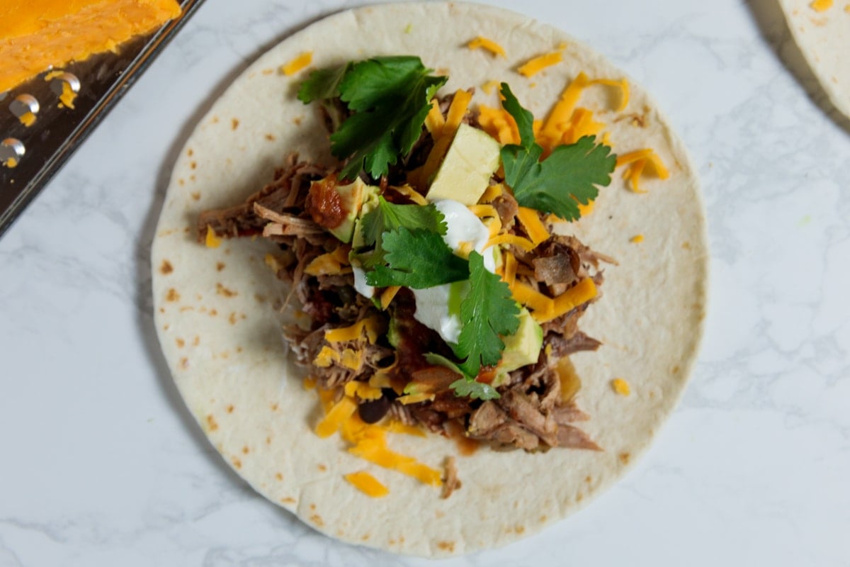 Marble surface with flour tortilla with carnitas meat.