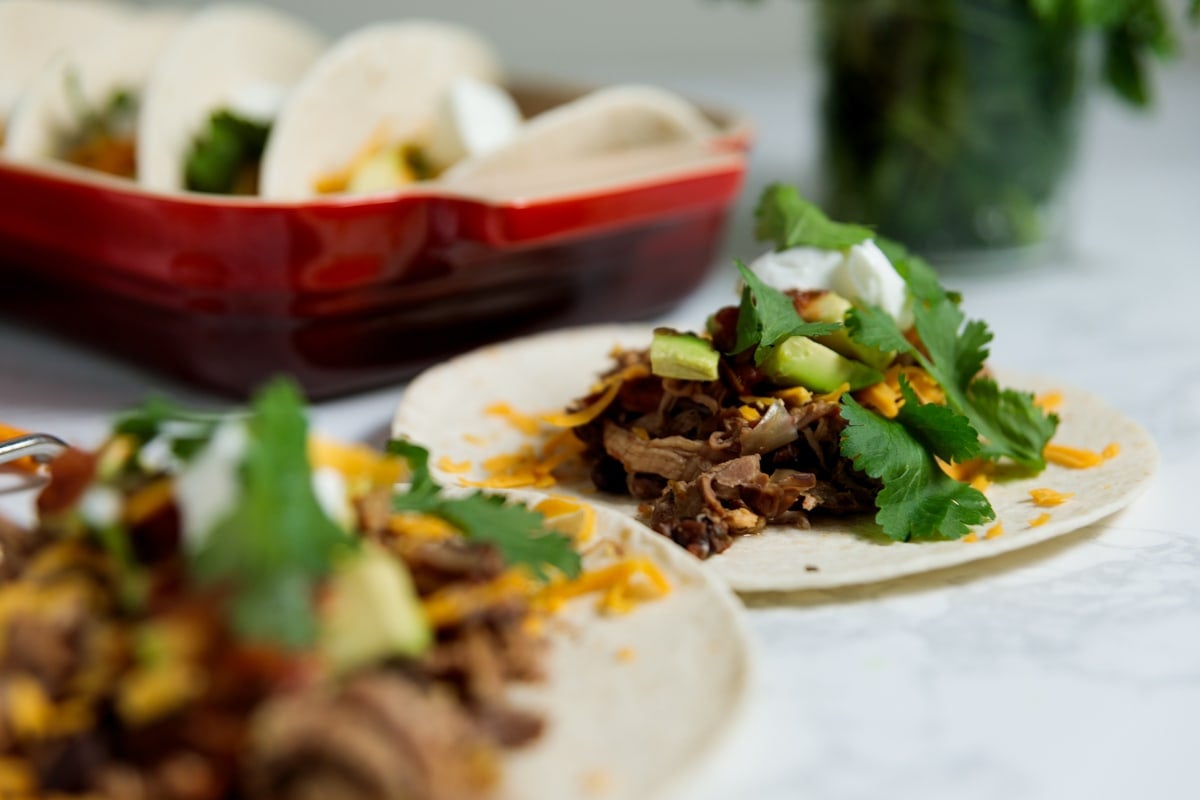 Slow cooker carnitas tacos with cilantro and avocado on marble surface.