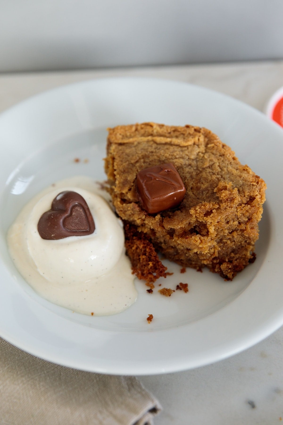 Piece of peanut butter cake with slightly melted chocolate candy on top with scoop of ice cream to the side ready to be eaten.