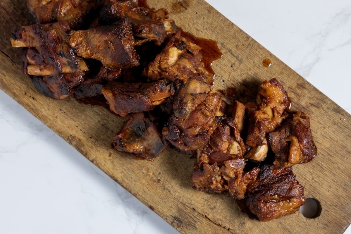 White marble surface with wooden cutting board with short ribs on top with bbq sauce drizzled all over.