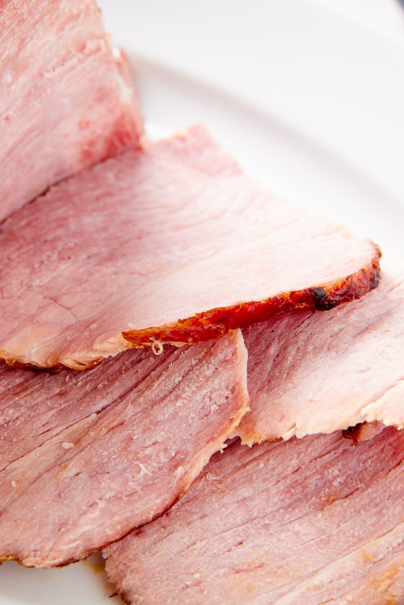 Slices of ham laying on top of each other showing texture of the meat all on white serving platter.