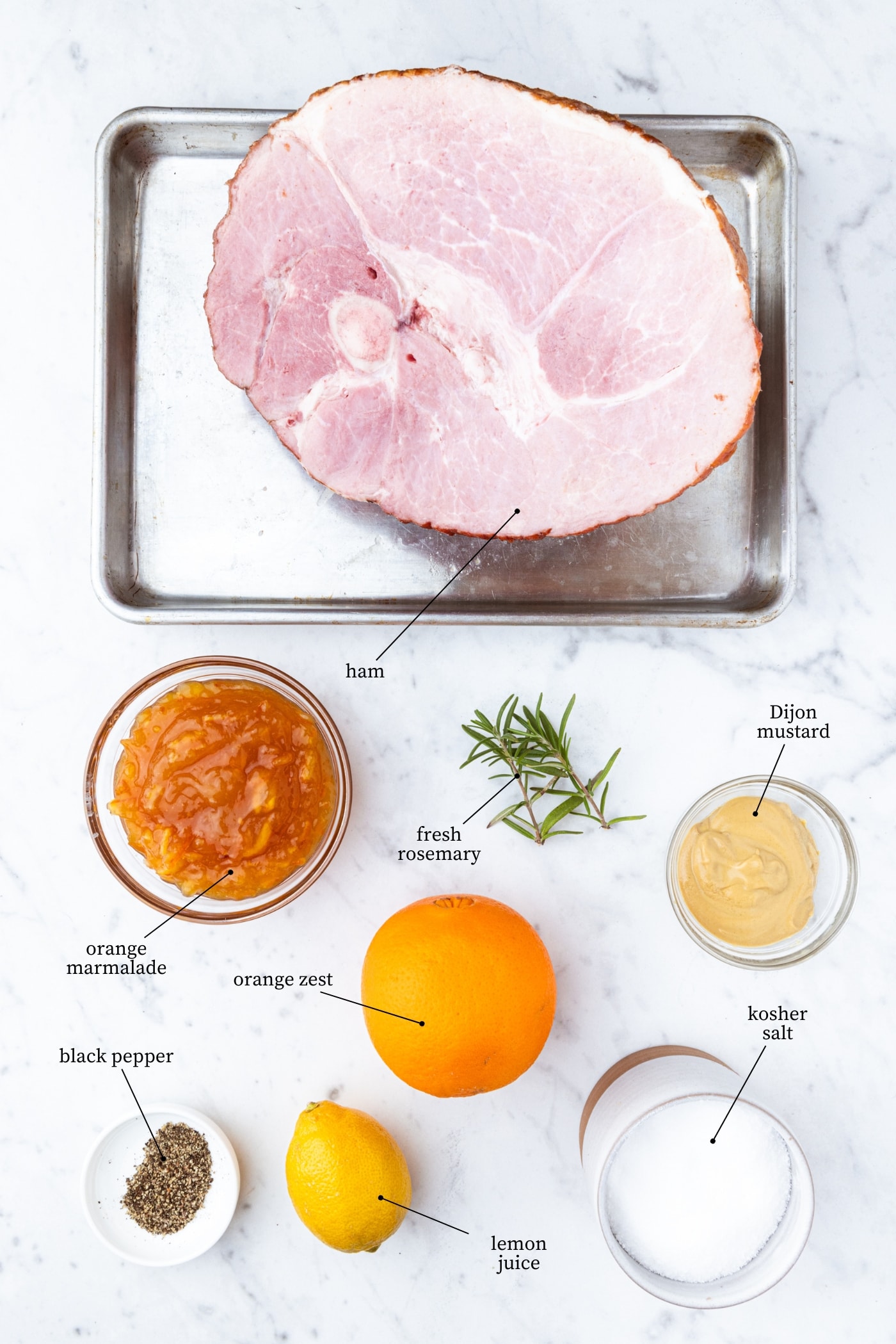 White marble surface filled with all ingredients needed for citrus glazed ham including ham, orange and lemon, Dijon mustard, and more.