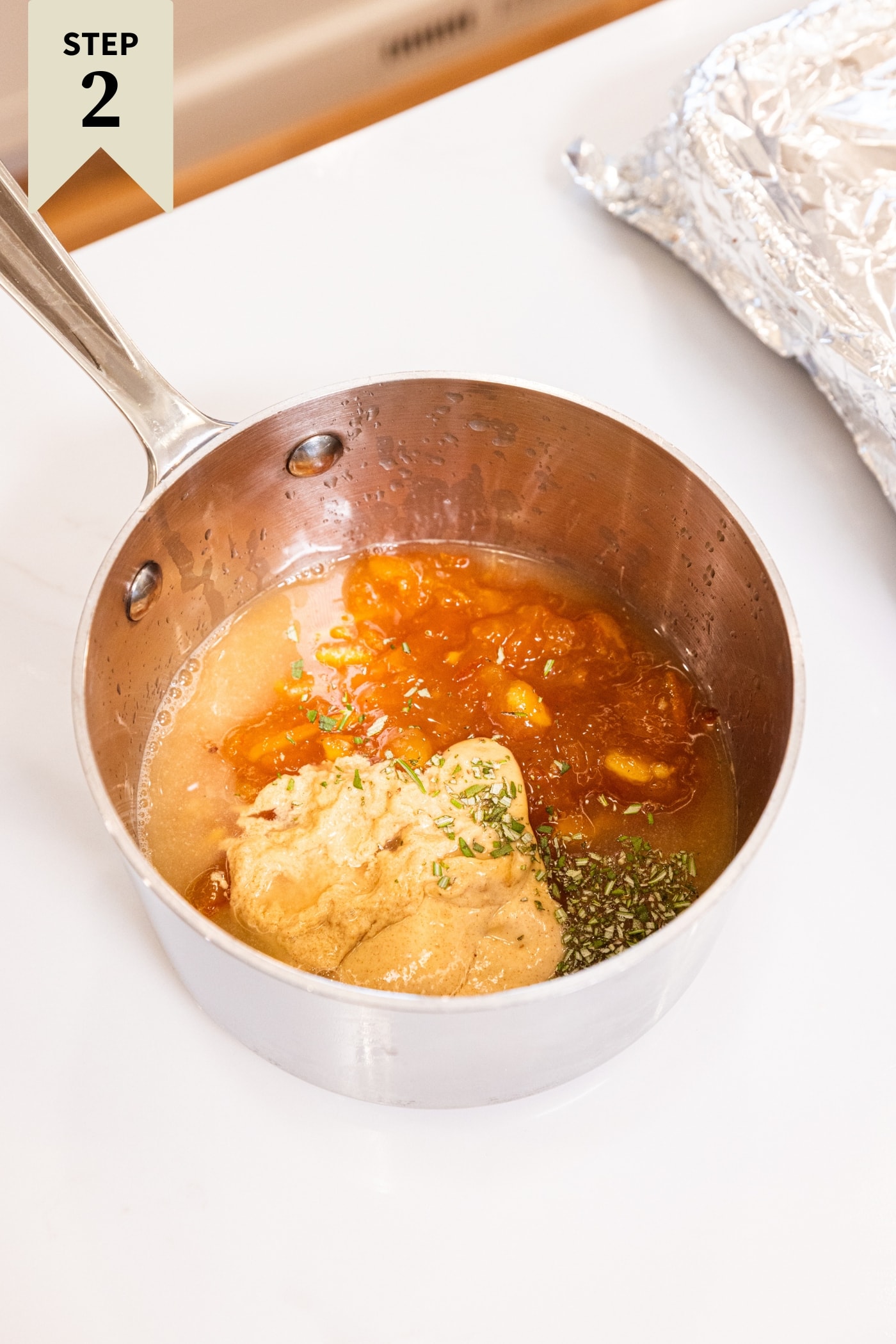 Small saucepan filled with all ingredients needed for an orange marmalade glaze including mustard, citrus juice, and more.