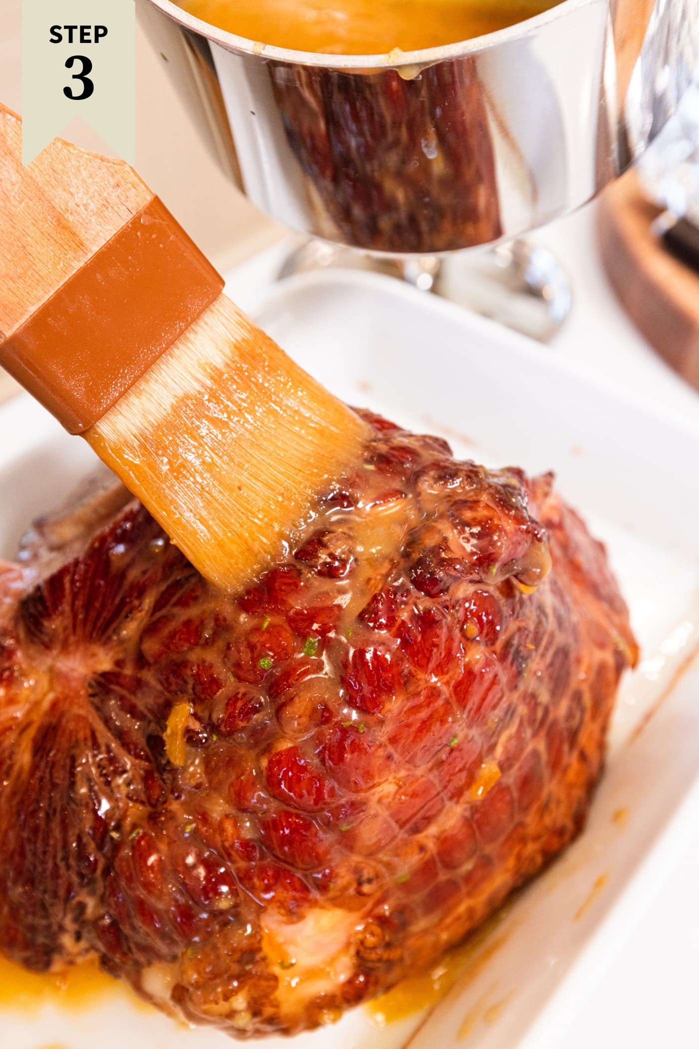 Brush brushing citrus glaze on top of warmed ham after being in the oven to initially warm through.