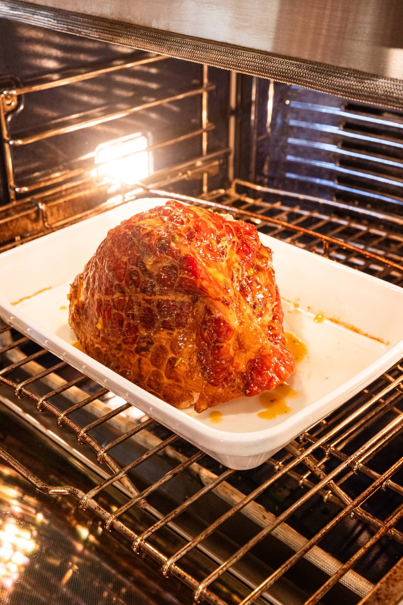 Ham covered in citrus glaze in a white baking dish being placed back into the oven to finish heating.