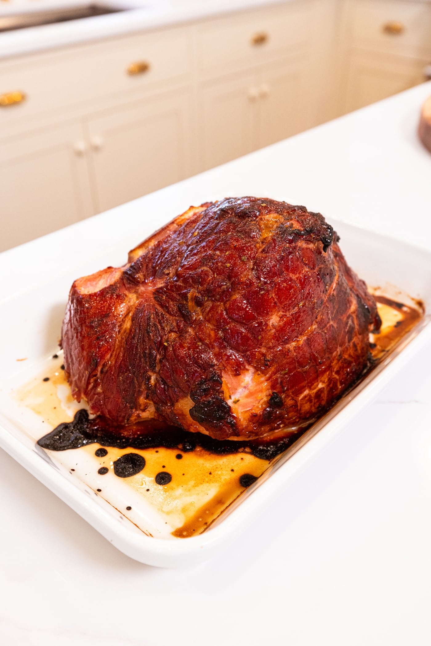 Ham sitting in white baking dish with citrus glaze all over the top after coming out of the oven once it reached the correct temperature.