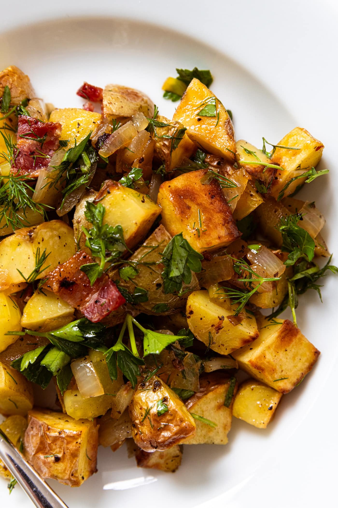 White plate filled with German potato salad with herbs all over the top showing crisp edges of the potatoes.